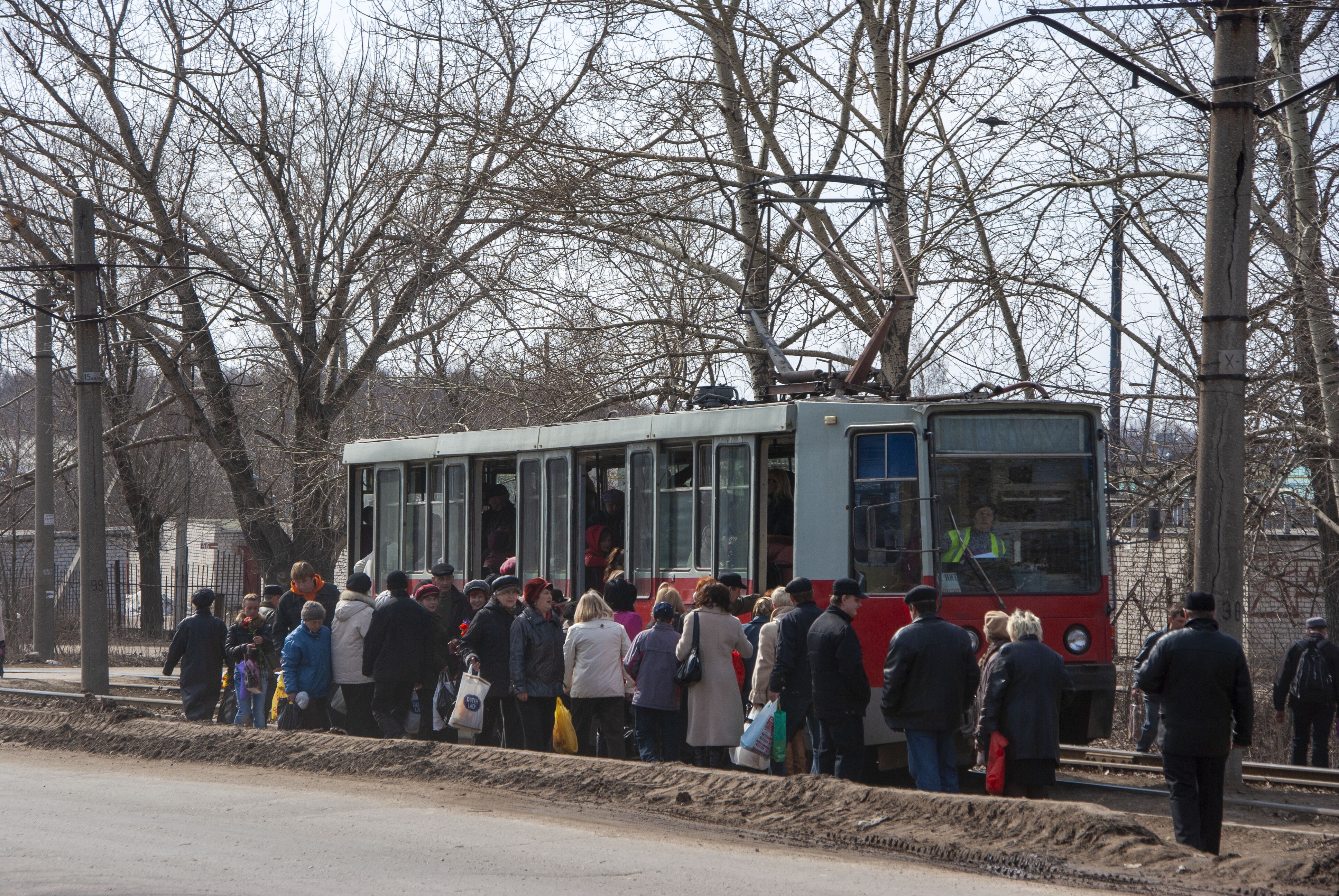 Пассажиры с кладбища стоят на остановке у заполненого трамвая
